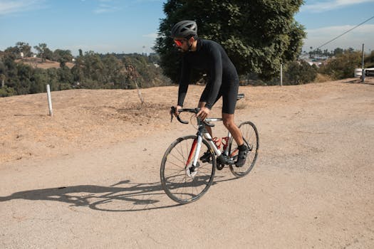 A cyclist wearing a helmet and sunglasses rides a bike on a sunny day in a natural setting.