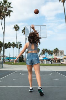 A woman in denim shorts plays basketball at an outdoor court during summer.