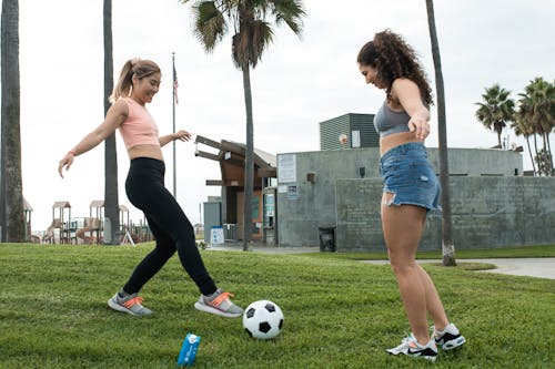 無料 白いサッカーボールを保持している灰色のタンクトップと青いデニムのショートパンツの女性 写真素材