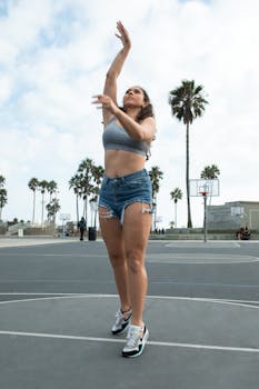 Athletic woman shooting hoops in outdoor basketball court with palm trees.