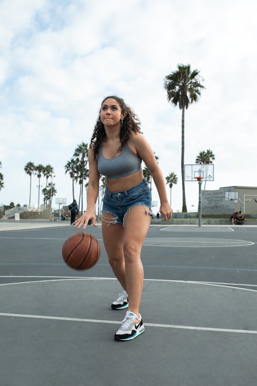 免費 藍色牛仔短褲和白色背心舉行籃球的女人 圖庫相片