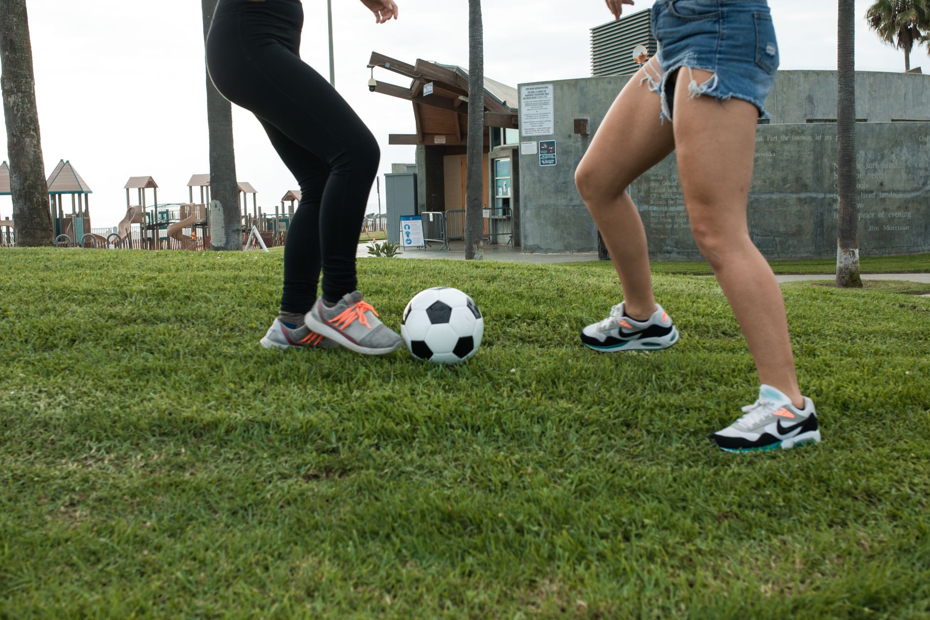 Two women playing soccer on grass in a park setting, emphasizing physical activity.