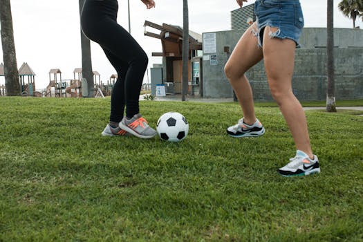Two women playing soccer on grass in a park setting, emphasizing physical activity.