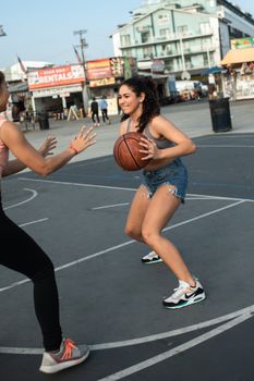 Two women enjoying a basketball game on an outdoor court, showcasing fun and active lifestyle.
