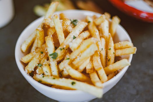 Golden crispy french fries sprinkled with parsley in a white bowl.