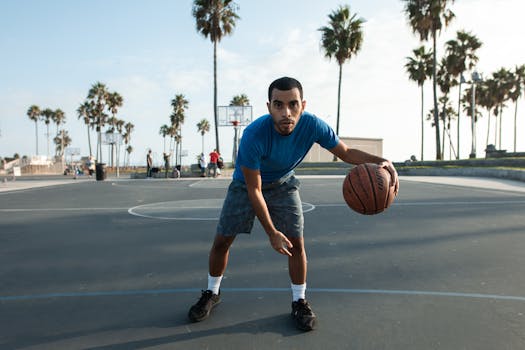 A young man dribbling a basketball on an outdoor court with palm trees in the background.