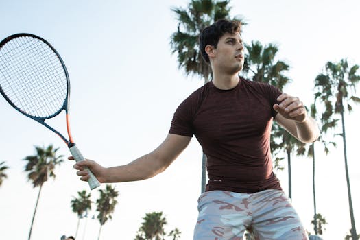 Athlete playing tennis on an outdoor court surrounded by palm trees.