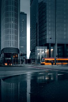 Dark and moody urban scene with reflections, skyscrapers, and a tram in Warsaw, Poland.