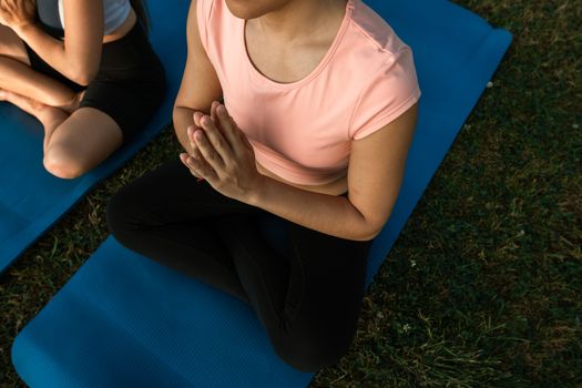 Two women practicing yoga in anjali mudra on blue mats outdoors, promoting wellness.