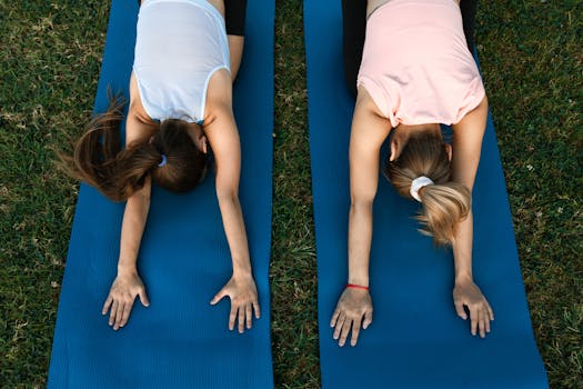 Two women practicing yoga in child's pose on blue mats outdoors. Ideal for fitness and relaxation themes.