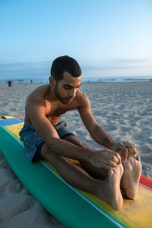 A Man Stretching over a Surfboard
