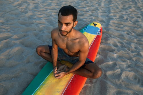 Topless Mężczyzna Siedzi Na Czerwony I żółty Deska Surfingowa Na Plaży
