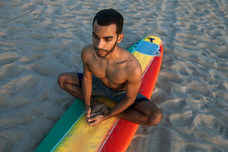 A Man Meditating Over A Surfboard On The Beach Sand