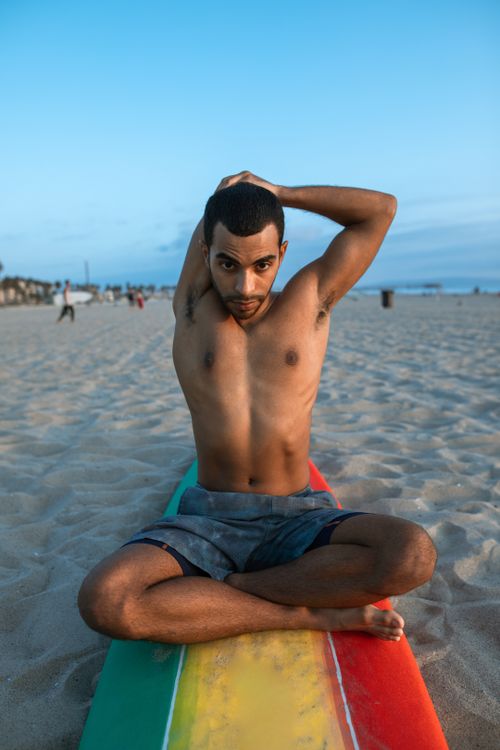 Free A young man stretches on a vibrant surfboard at the beach during sunset, focusing on wellness. Stock Photo