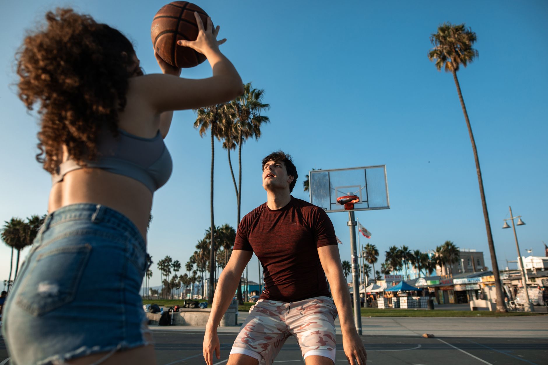 Young adults playing basketball on an outdoor court surrounded by palm trees.