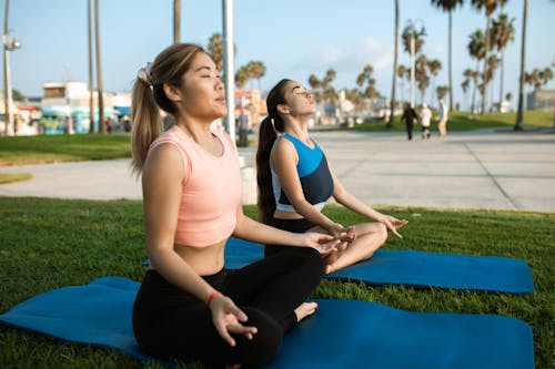 粉色背心和黑色緊身褲，坐在藍色瑜伽墊上的女人