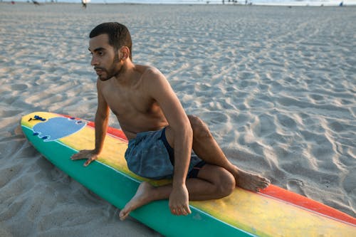 Mężczyzna W Niebieskich Spodenkach Siedzi Na Niebieskim Desce Surfingowej Na Plaży