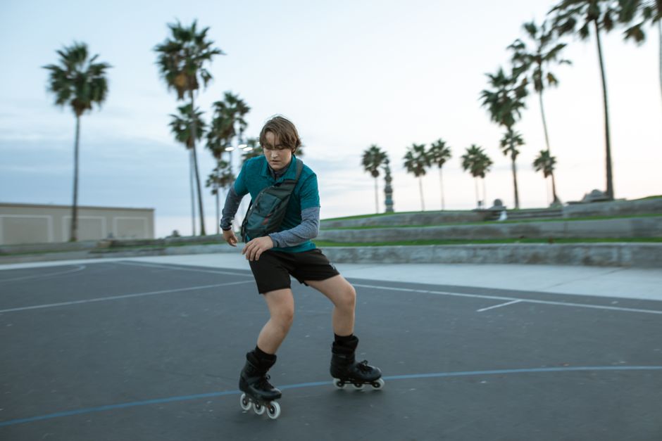 Energetic young man rollerblading on a sunny day in an outdoor park with palm trees.