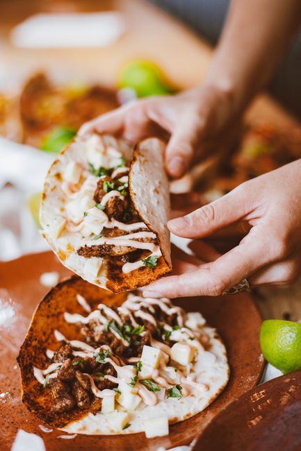 Fotomural Primer plano de manos sosteniendo un delicioso taco con carne, salsa cremosa y un limón al lado.