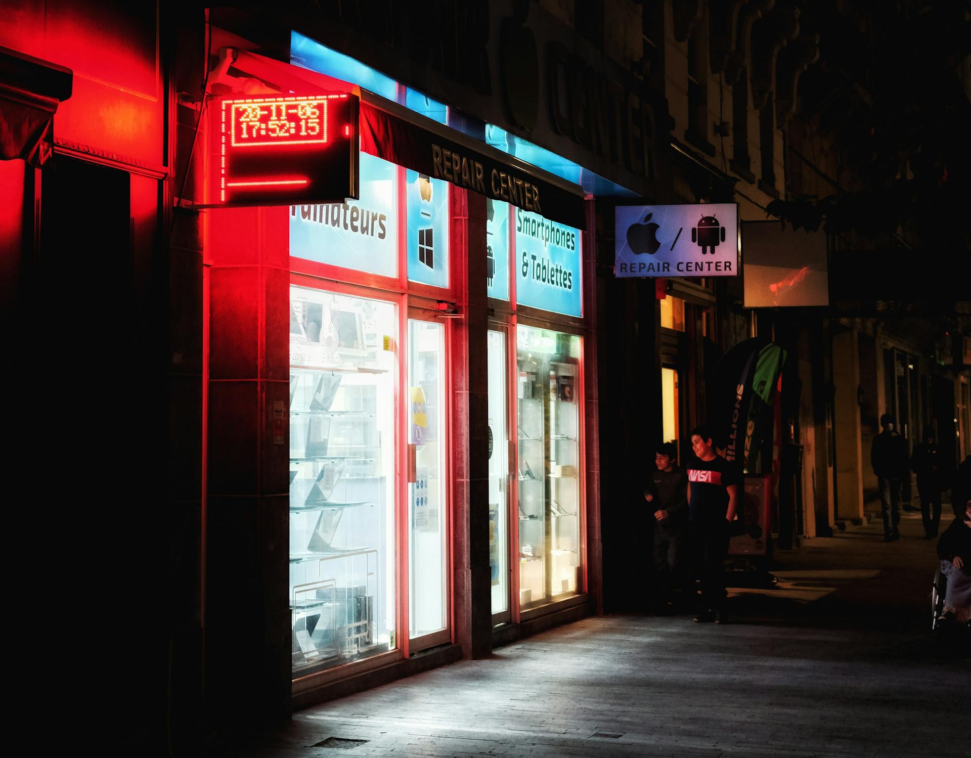 Vibrant night scene of an illuminated smartphone repair store with red signage.