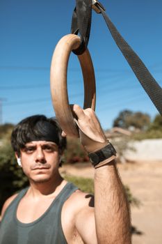 Man practicing with gymnastics rings outdoors under blue sky, showcasing fitness and strength.