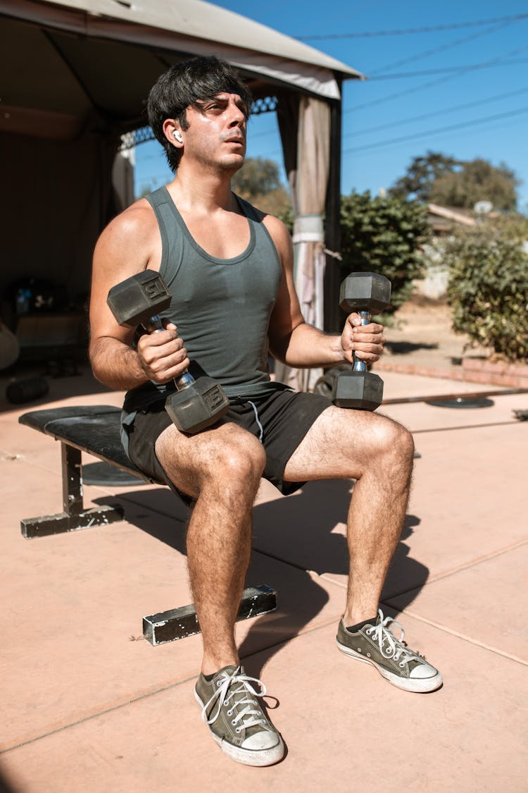 Man Sitting On Bench While Holding Dumbbells