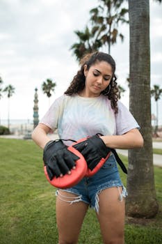 Woman adjusting boxing mitts outdoors, highlighting active lifestyle amidst palm trees.