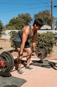 Man doing deadlift in an outdoor setting under clear blue sky.