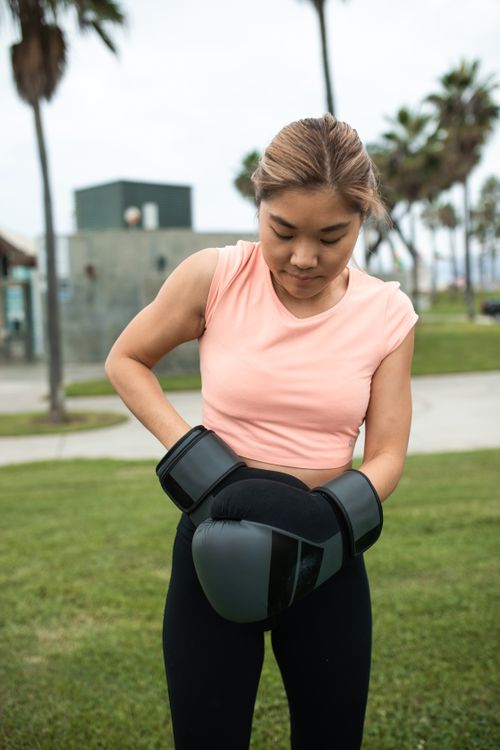 Free A woman in sportswear at an outdoor park putting on boxing gloves. Stock Photo