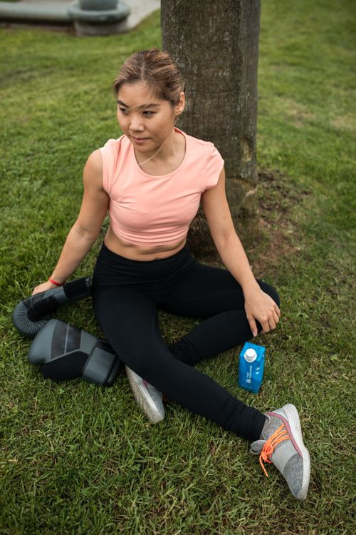 Free A woman takes a break after exercising outdoors, sitting on grass with a drink. Stock Photo
