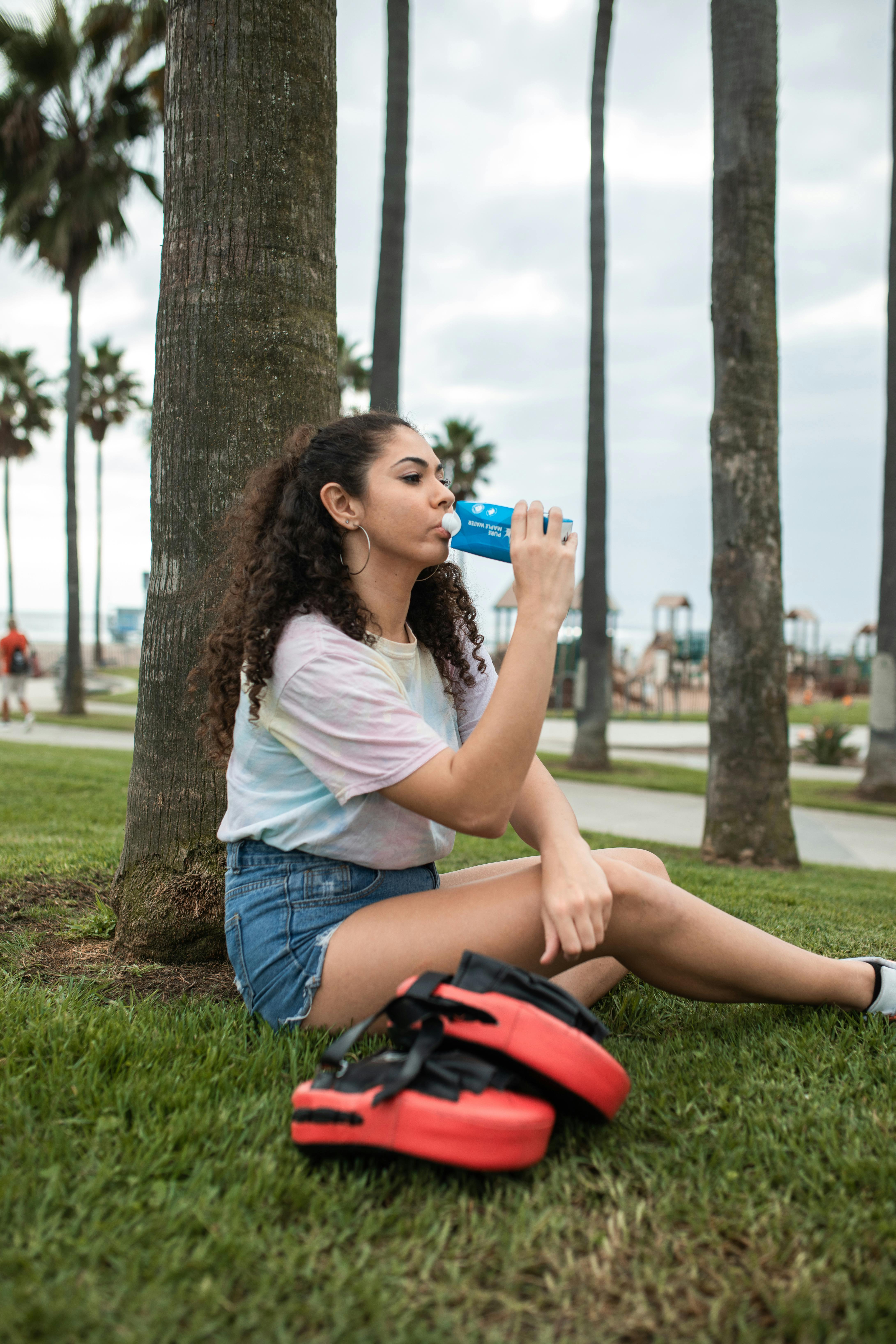 brunette woman drinking maple water and sitting by tree