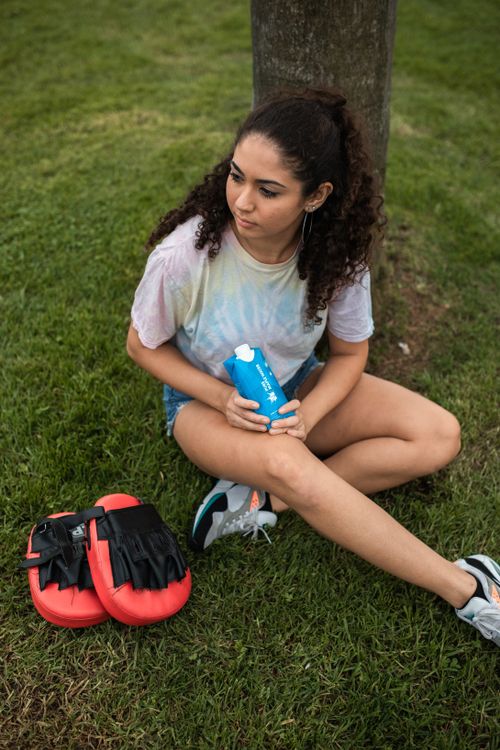 Free Young woman sitting on grass with sports gear, enjoying a moment outdoors with a drink. Stock Photo