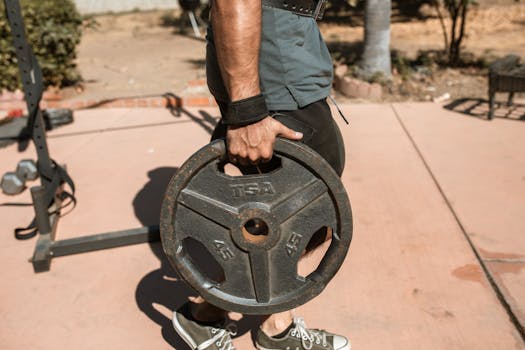 Close-up of a man's hand holding a 45lb weight plate outdoors during exercise.