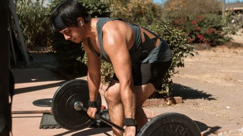A man lifting a barbell outdoors, emphasizing strength and fitness in a sunny setting.