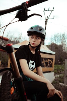 A young woman wearing a helmet sits resting next to her bicycle in an outdoor setting.