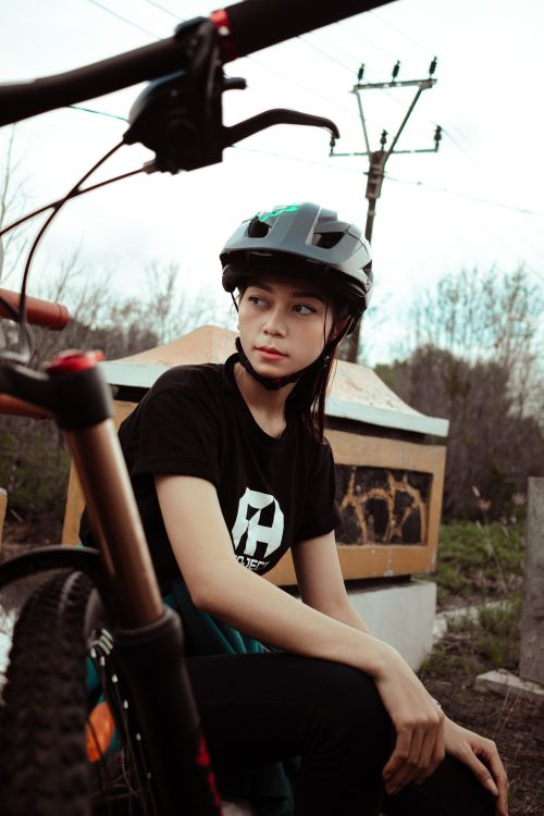Free A young woman wearing a helmet sits resting next to her bicycle in an outdoor setting. Stock Photo