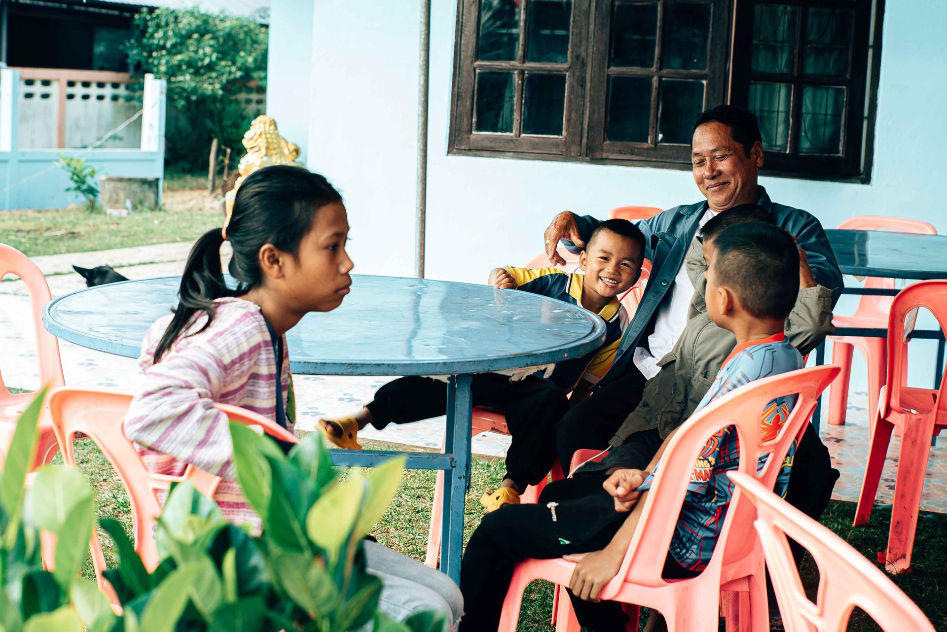 A joyful family gathering outside a home in Thailand, featuring smiling adults and children.