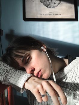 一位忧郁的女性戴着耳机听音乐，在房间里靠着胳膊坐在玻璃旁