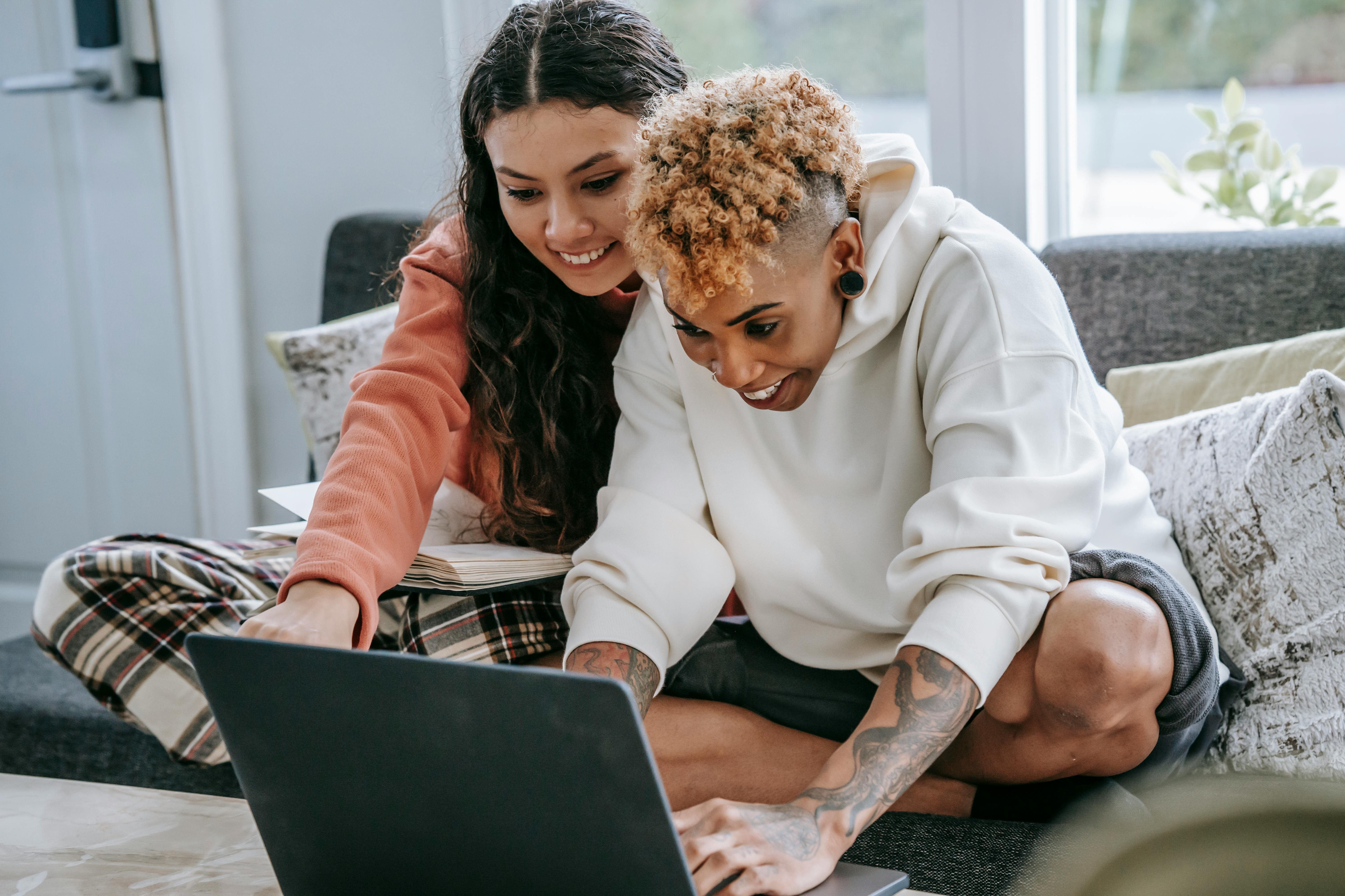 crop smiling multiethnic girlfriends surfing internet on laptop on sofa