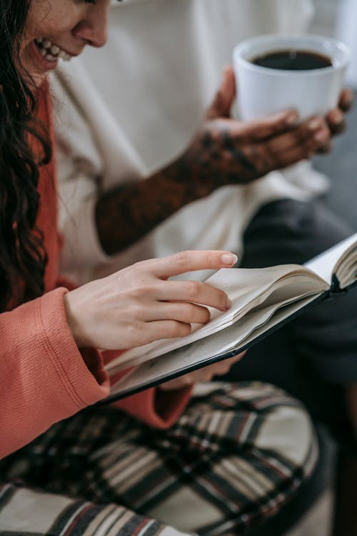 Femme Joyeuse Avec Livre Près De Partenaire Ethnique Méconnaissable Avec Boisson