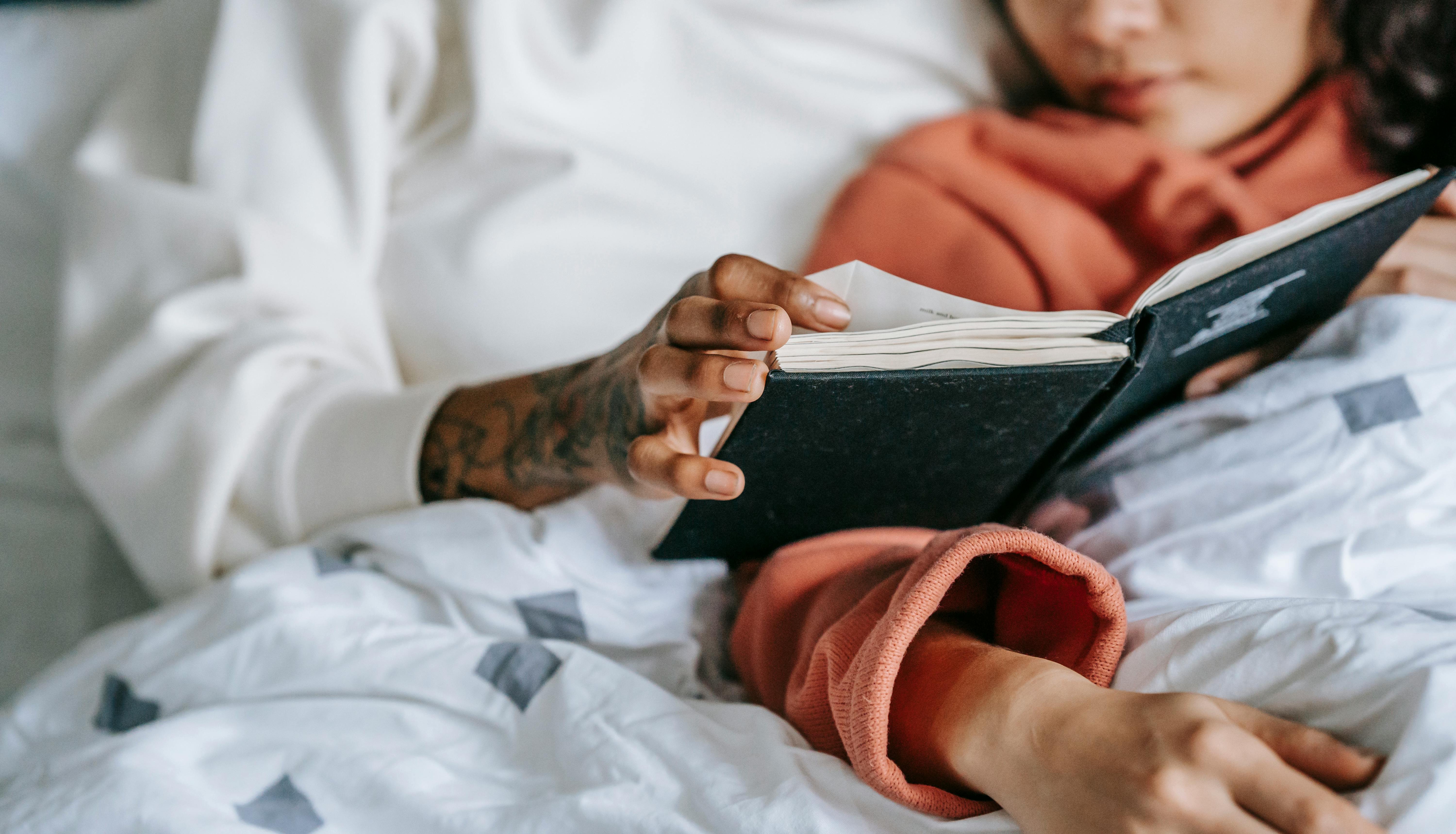 crop homosexual diverse couple of women reading book in bed