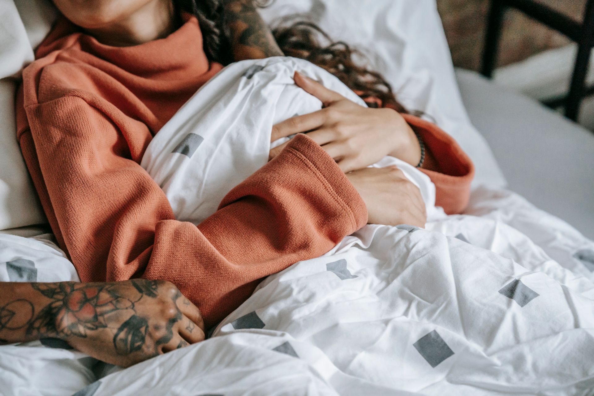 From above of crop female resting in bed under crumpled duvet with anonymous black beloved in house