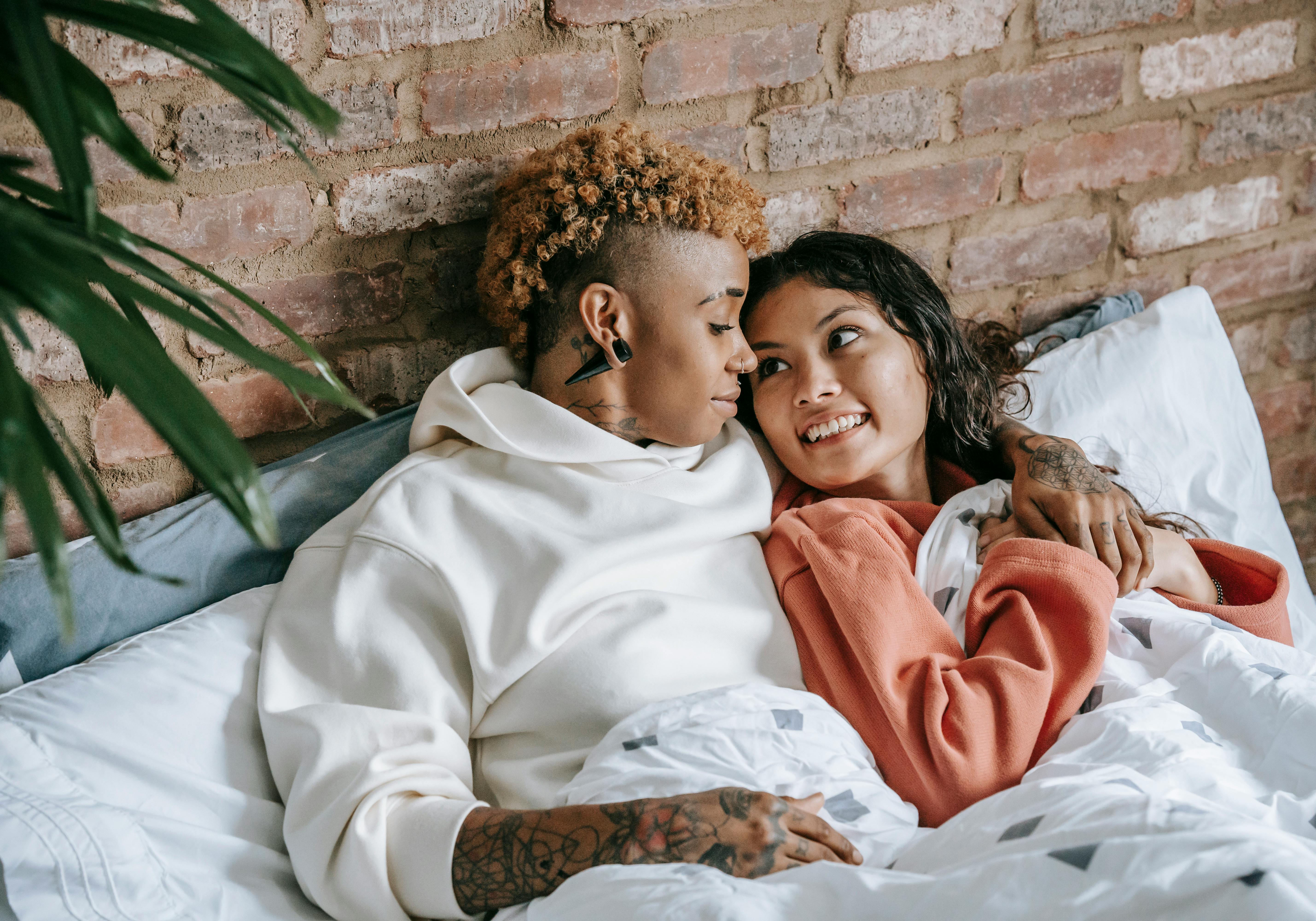 smiling homosexual diverse women cuddling in bed at home