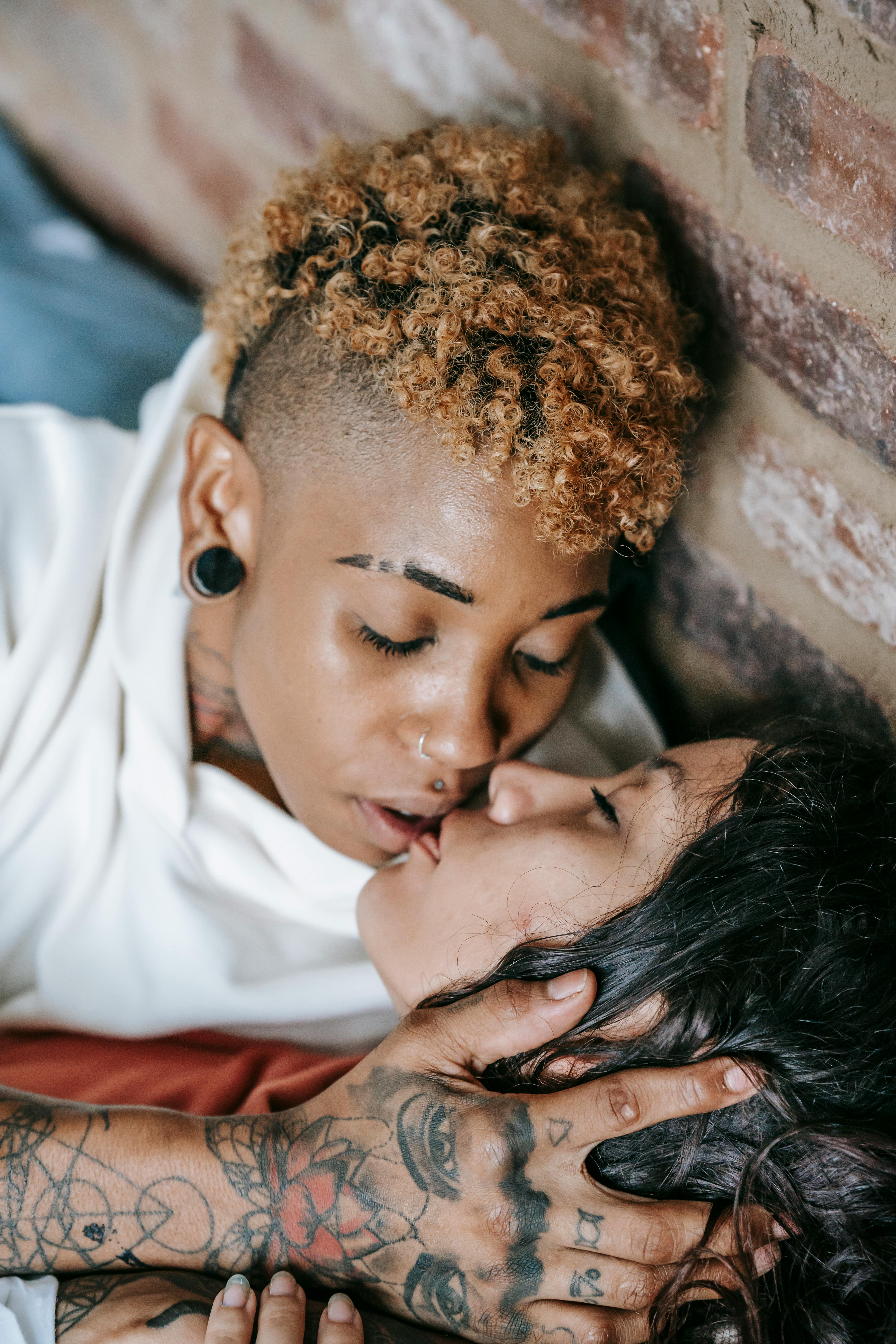 sensitive multiracial lesbian couple kissing near brick wall