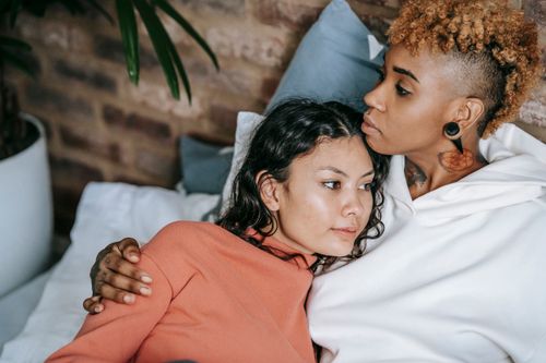 Free Crop dreamy black woman with punk hairstyle cuddling homosexual ethnic girlfriend while lying on bed and looking away Stock Photo