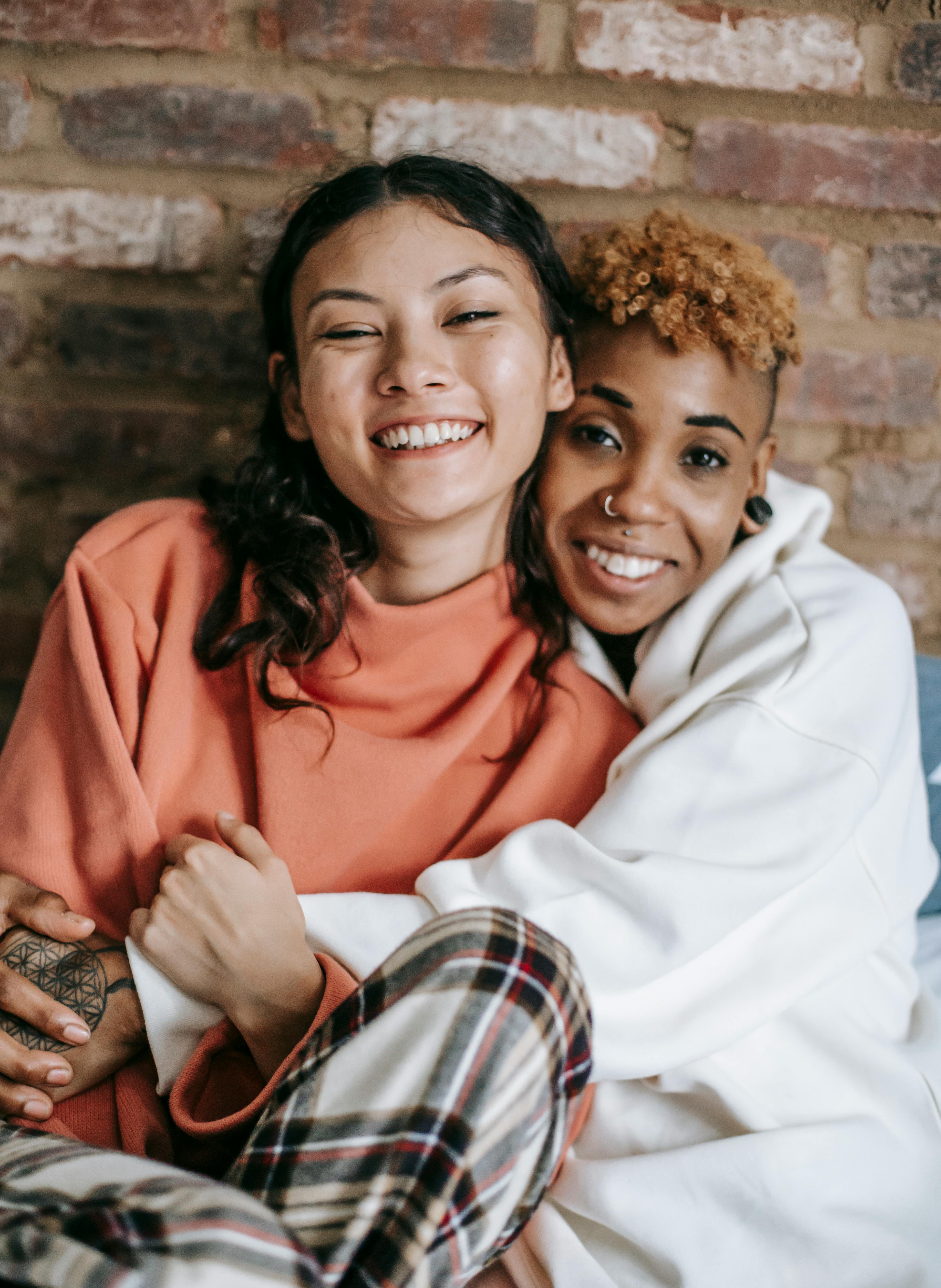 happy diverse lesbian couple embracing near brick wall