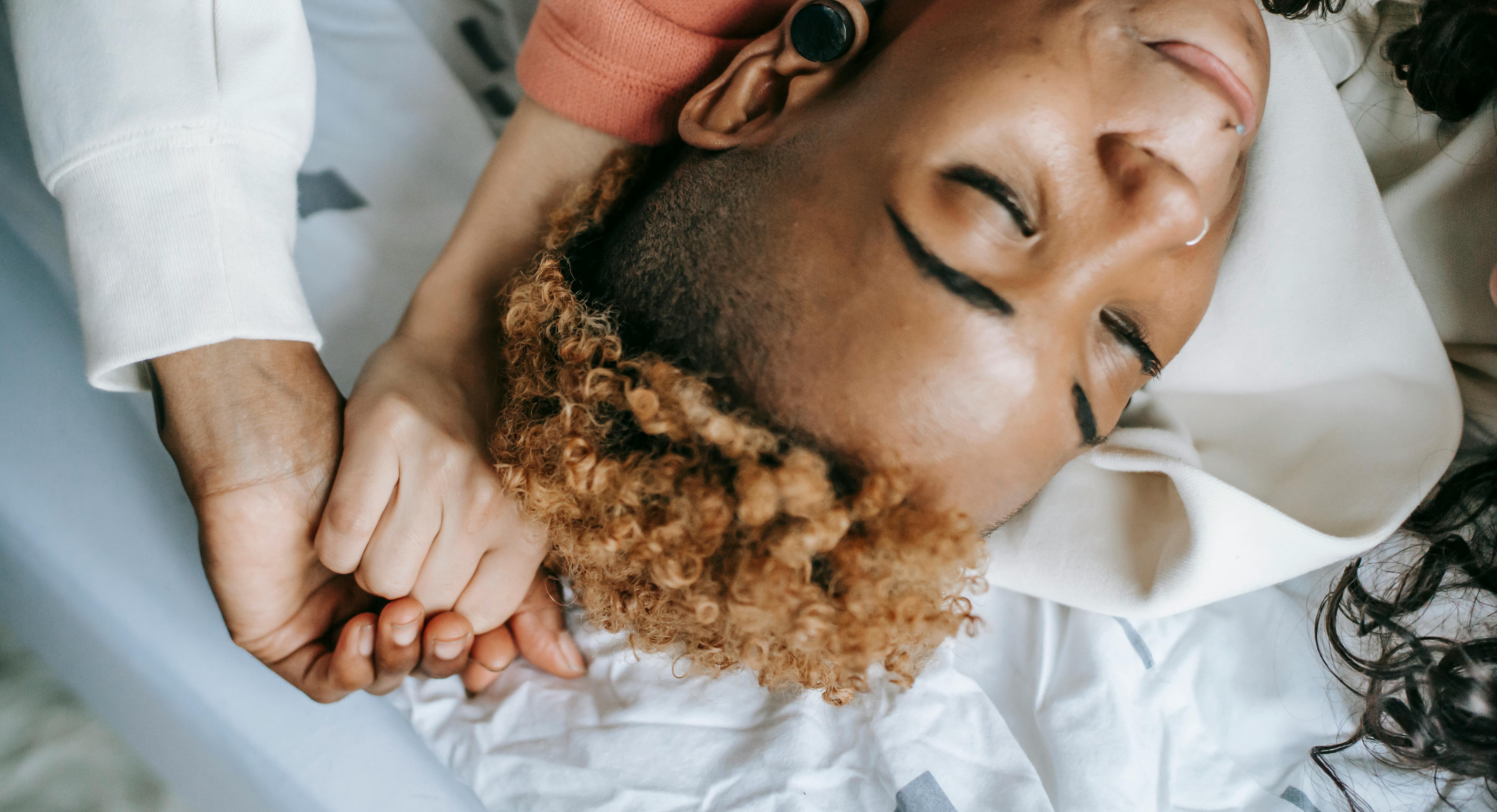 crop black woman resting on bed and holding girlfriends hand