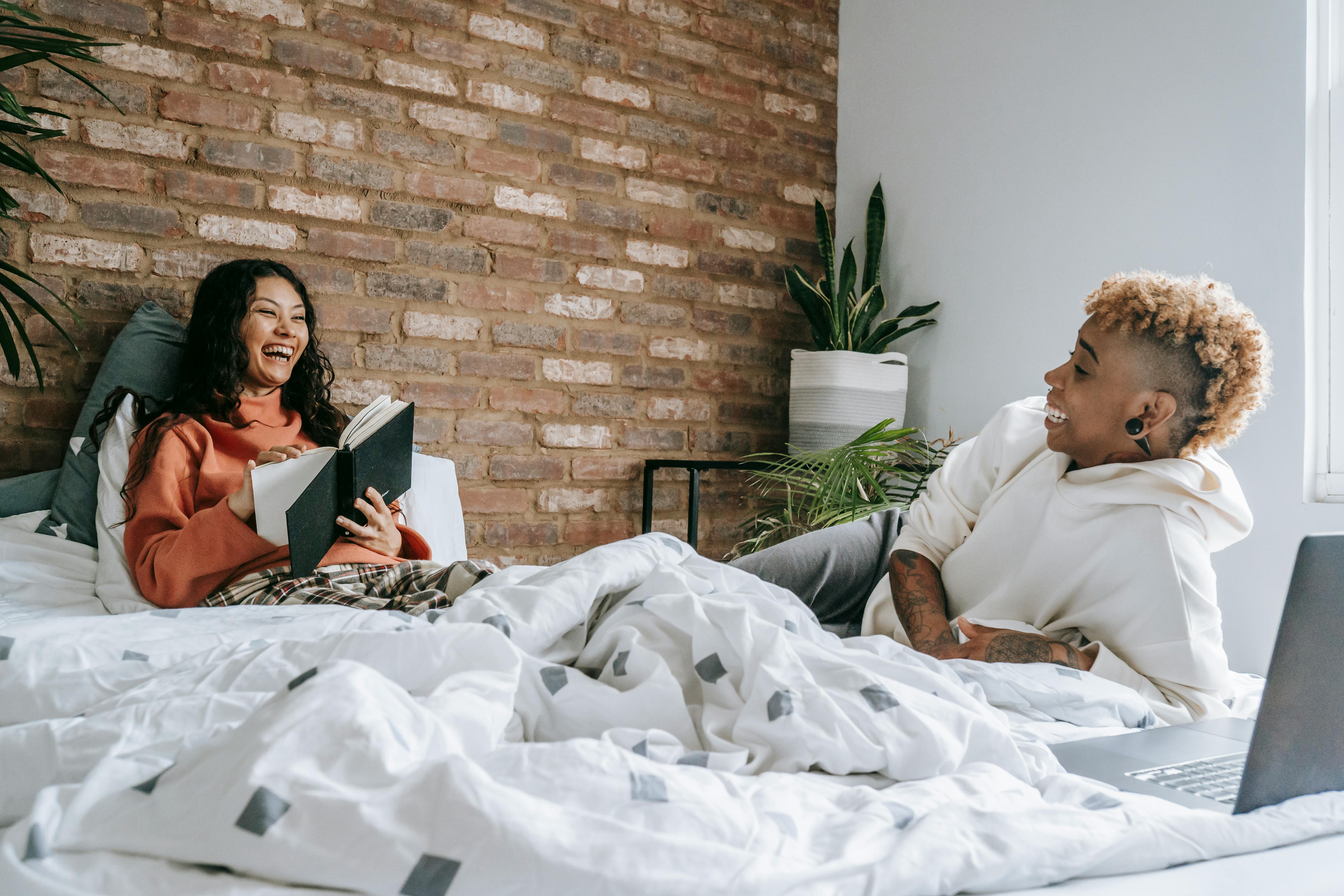 joyful lesbian couple resting on bed with laptop and book