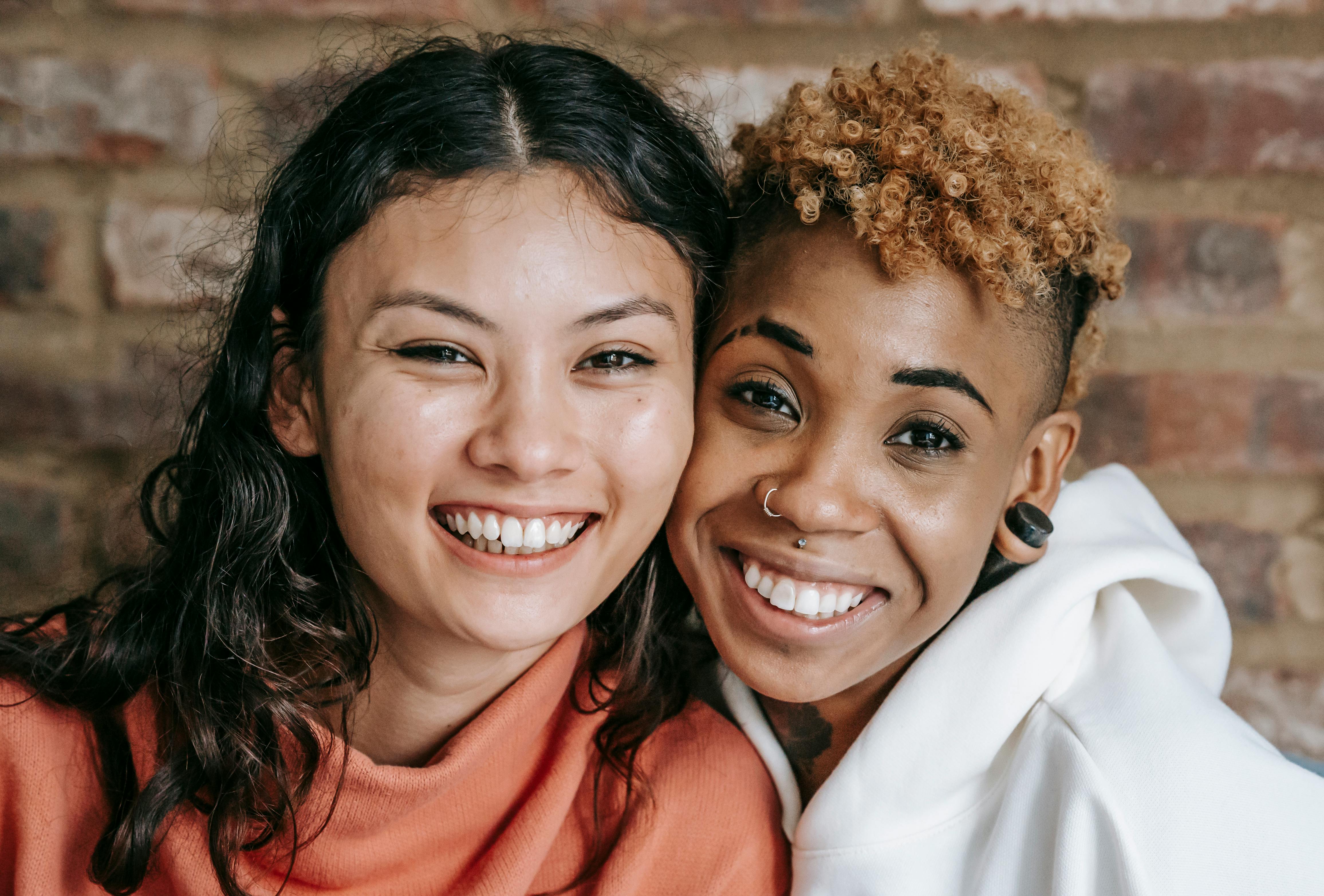 cheerful multiethnic lesbian couple embracing against brick wall