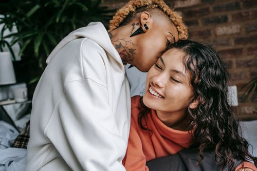Free Young African American informal female in casual outfit kissing content smiling girlfriends cheek while spending free time together at home Stock Photo
